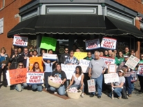 group of people with signs calling for health care reform posing for the camera in front of a store